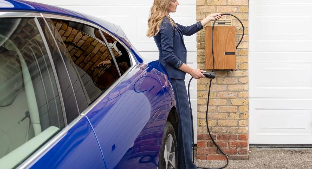 A woman efficiently charges her blue electric car at a home EV charging station.